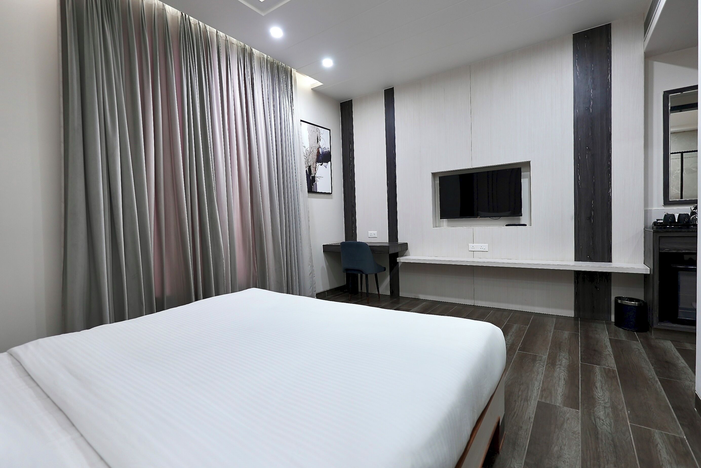 Ein modernes Hotelzimmer mit einem großen Bett, einem Schreibtisch mit Stuhl, einem flachbildfernseher an der Wand und einem kleinen Fenster.
