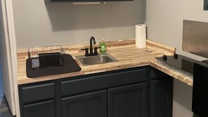 Une cuisine avec des meubles de couleur sombre, un plan de travail en bois, un évier et une cuisinière.