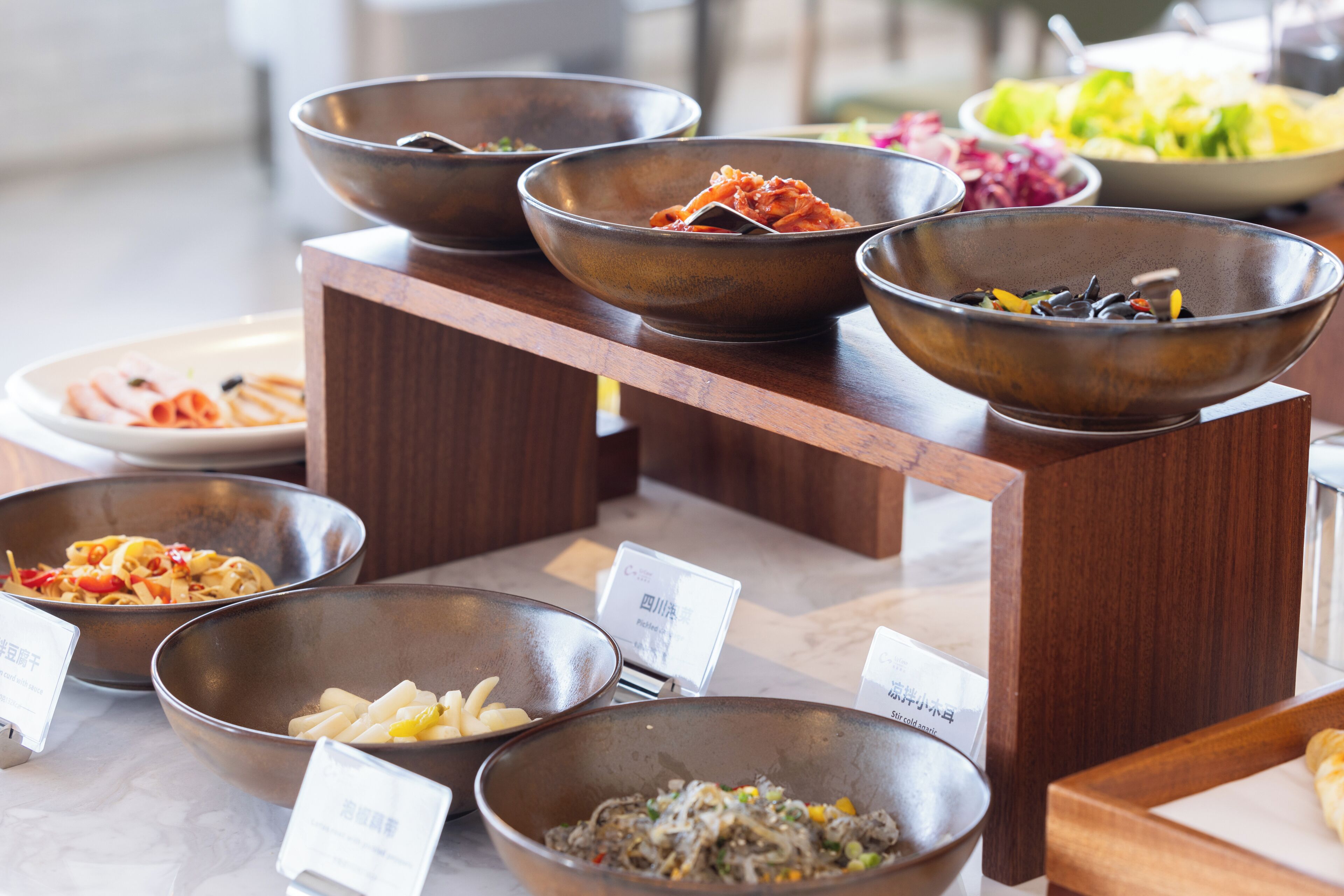 A buffet with various dishes in metal bowls, arranged on wooden stands.