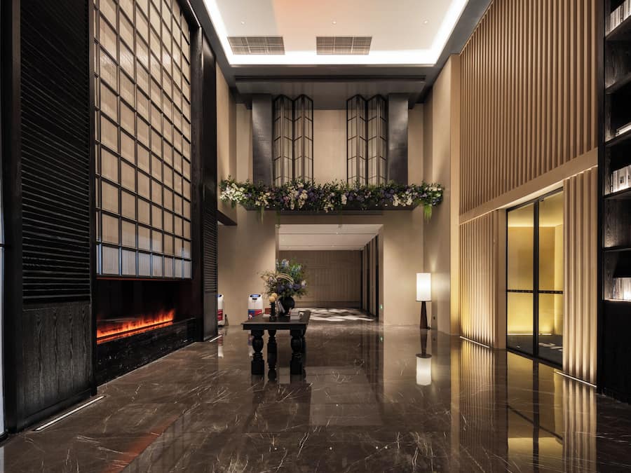 A modern lobby with a fireplace, a reception desk, and a bookshelf.