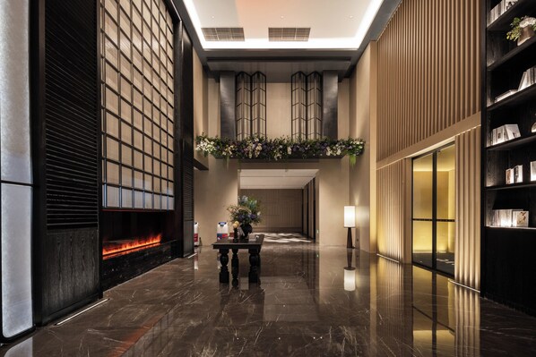 A modern lobby with a fireplace, a reception desk, and a bookshelf. - UrCove by Hyatt Guangzhou Huadu Baiyun International Airport (Guangzhou)