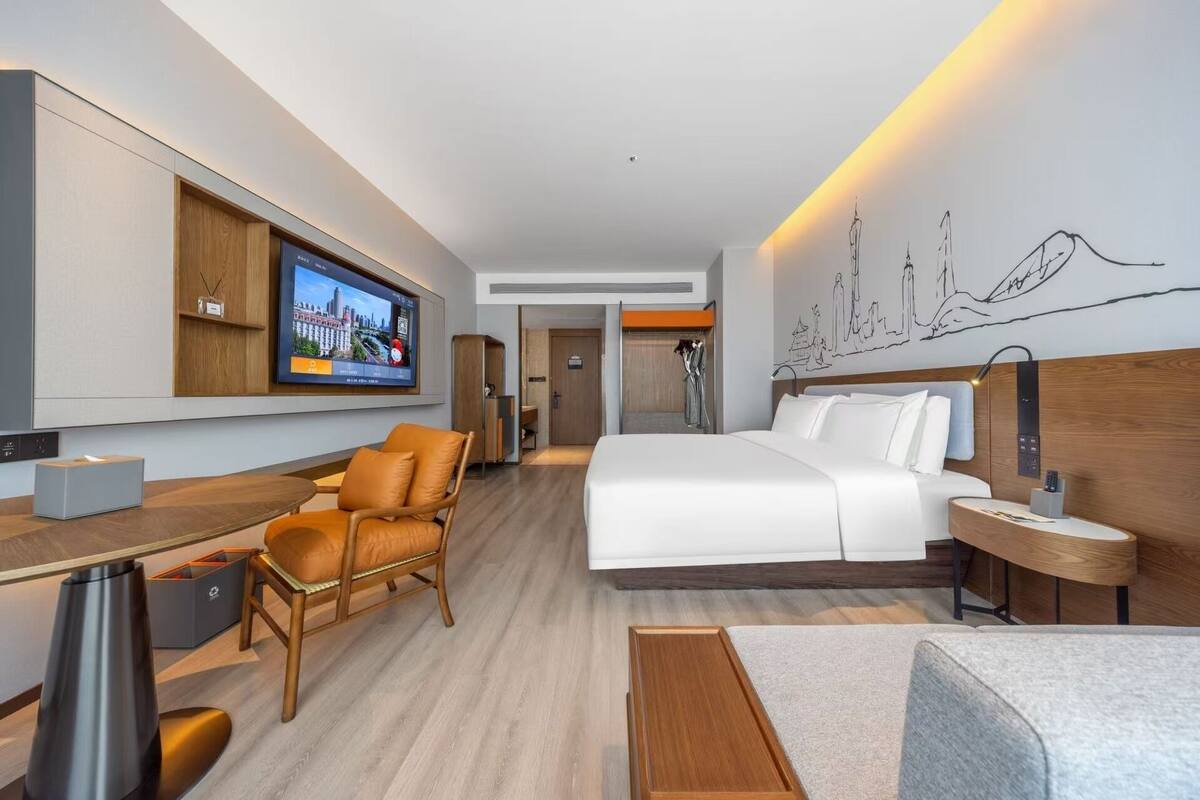 Ein Hotelzimmer mit Bett, Schreibtisch mit Fernseher, Sessel, Nachttisch und einer Wand mit Stadtbild-Fresko.