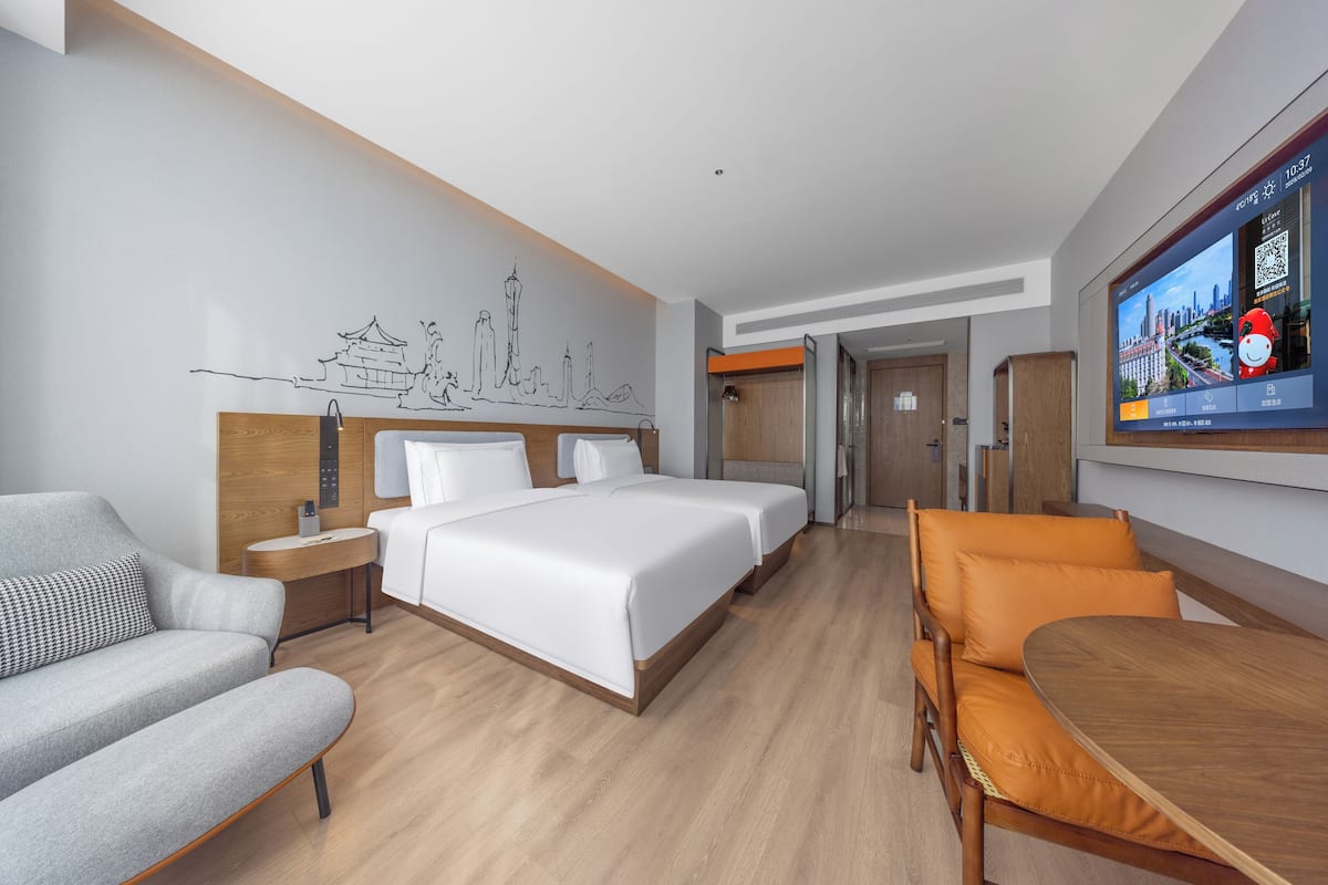 Ein modernes Hotelzimmer mit einem großen Bett, einer Couch, einem Esstisch und einem Fernseher, der eine Stadtansicht zeigt.