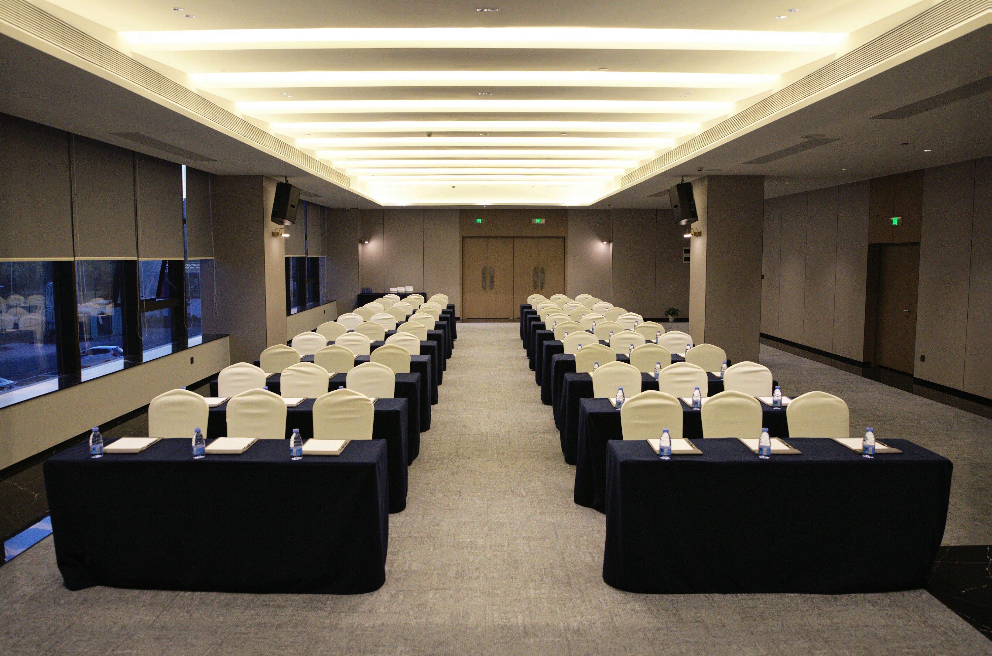 A conference room with rows of tables and chairs, large windows, and a high ceiling.