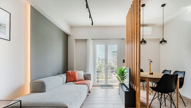 A modern living room with a sofa, a dining table with chairs, and a large window with a view of the city. - Brisk - Chic 1-BR Apartment in Athens (Athens)