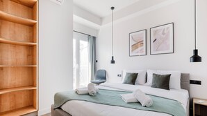 A modern hotel room with a large bed, a wooden shelf unit, a chair, and two framed artworks on the wall. - Brisk - Chic 1-BR Apartment in Athens (Athens)