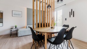 A modern dining area with a round wooden table, black chairs, and a vertical wooden partition. - Brisk - Chic 1-BR Apartment in Athens (Athens)