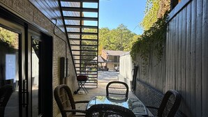 A patio with a glass table and wicker chairs, a metal pergola, and a view of a residential street. - Downtown+FreeParking+Wifi Main St. Ste 101 (Eureka Springs)