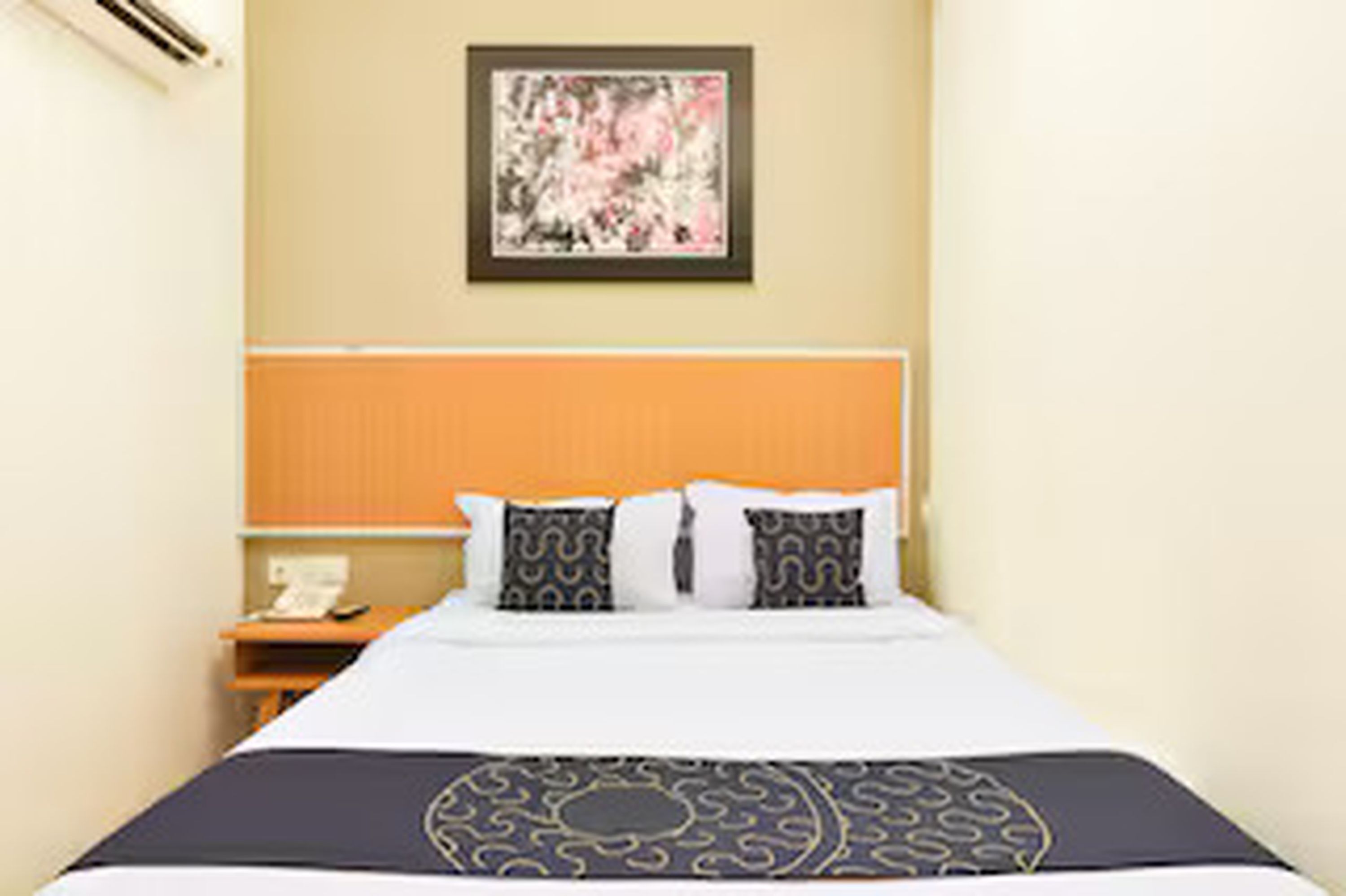 A hotel room with a bed, a nightstand, a telephone, and a painting on the wall.