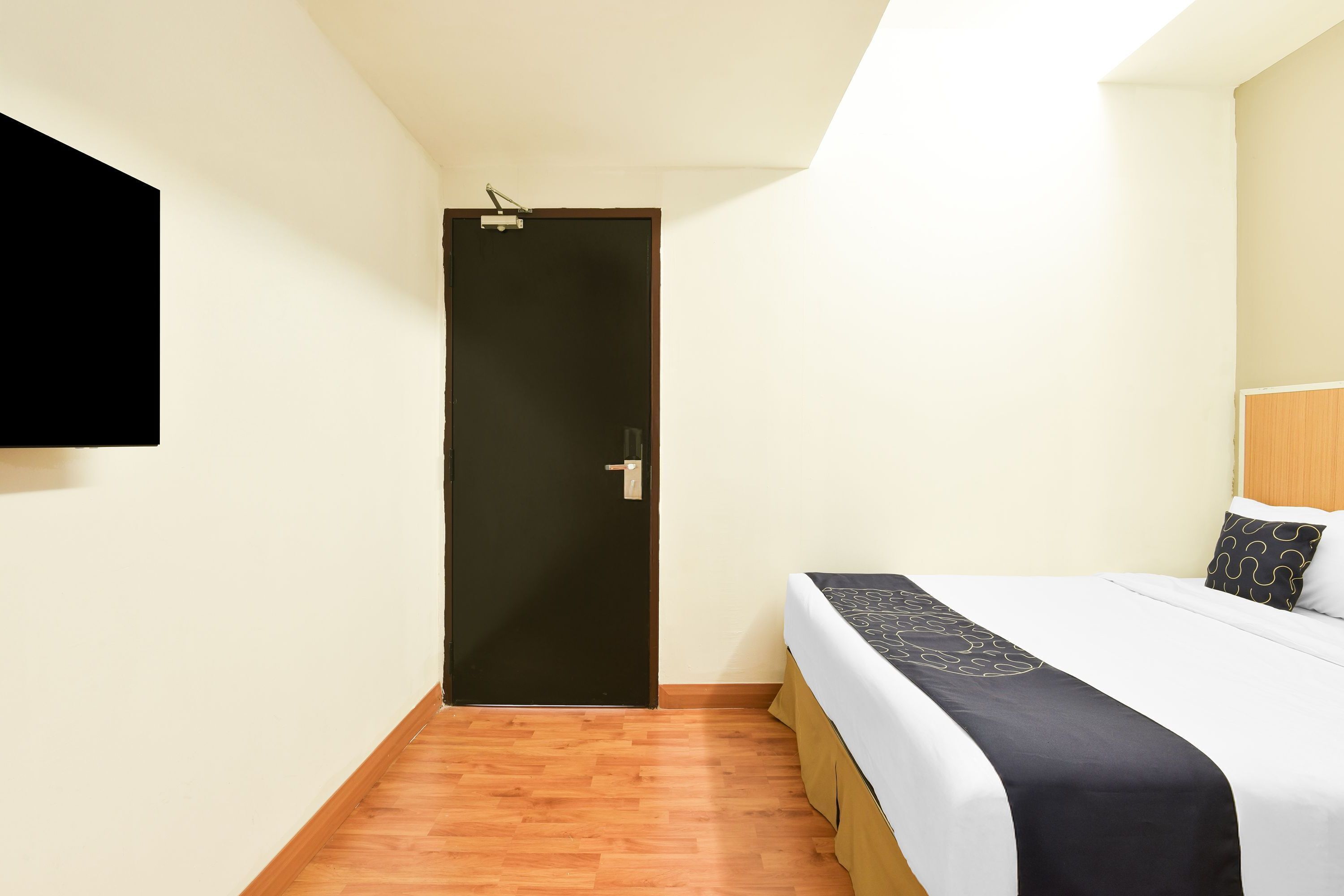A hotel room with a bed, a door, and a mounted television.