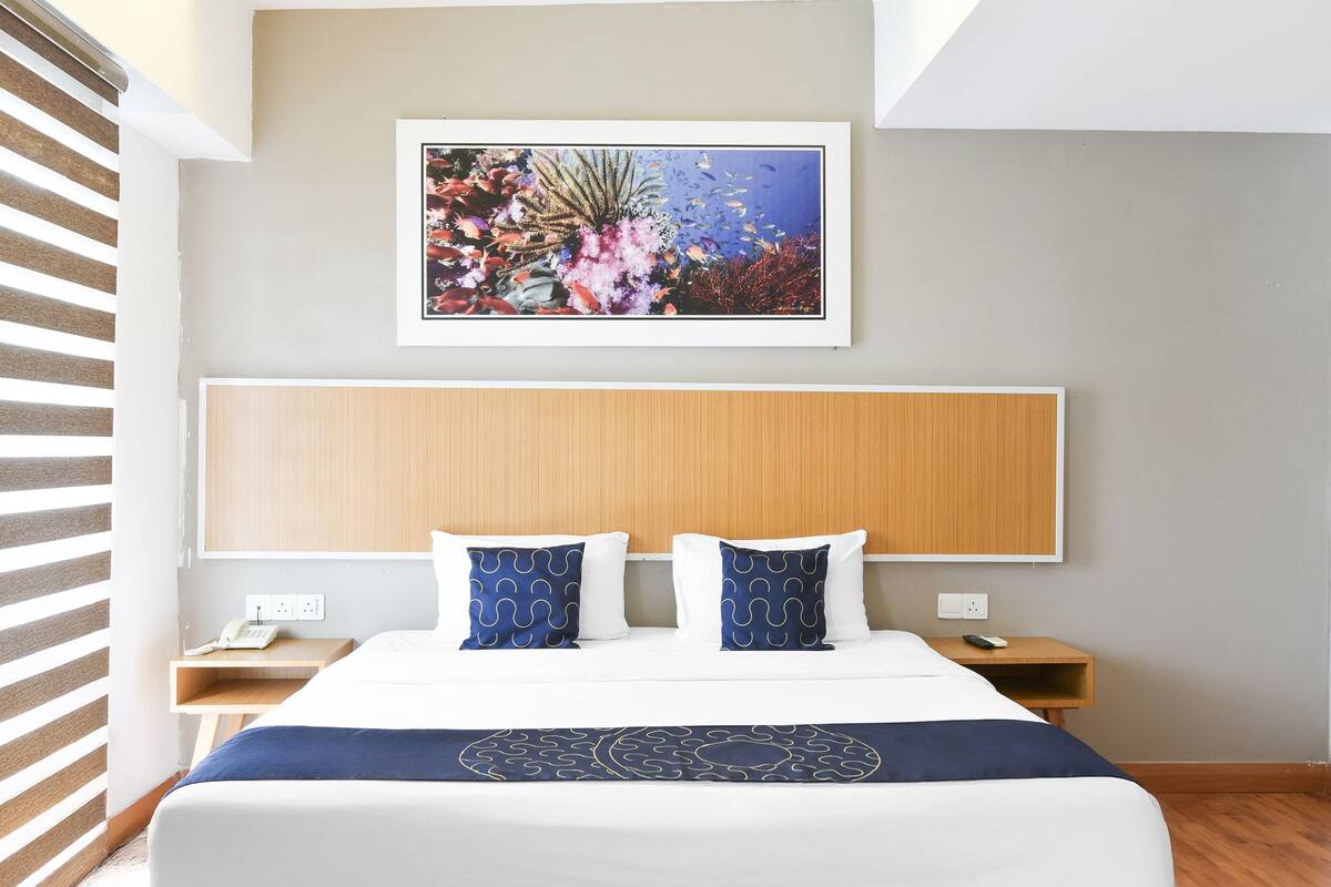 A hotel room with a bed, a headboard, a nightstand, a phone, and a framed picture of an underwater scene.