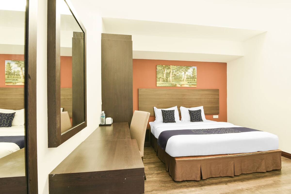 A hotel room with a large bed, a wooden desk, a chair, and a mirror.