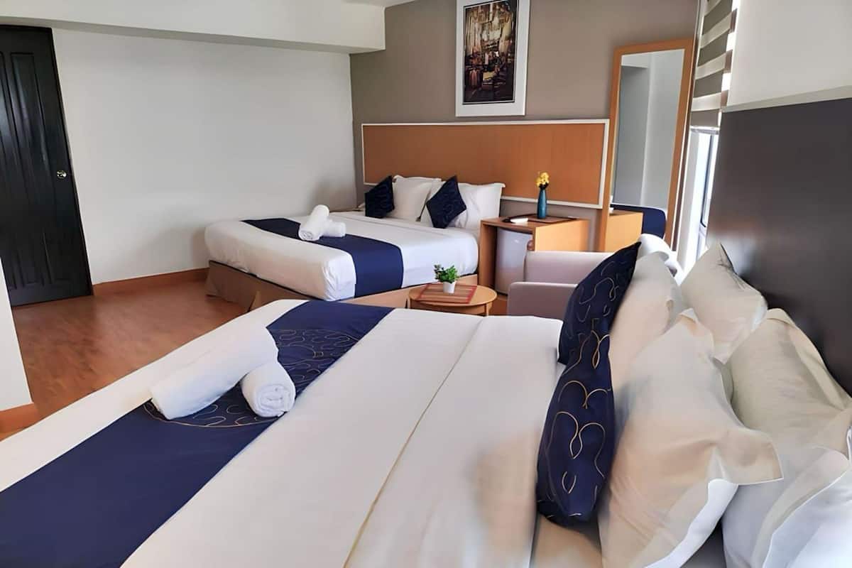 A hotel room with two beds, a bedside table with a lamp, a small table with a plant, and a large mirror on the wall.