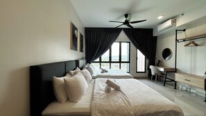A hotel room with a bed, a desk, a chair, a ceiling fan, and large windows. - Tulip Residences by Manhattan Group (Shah Alam)