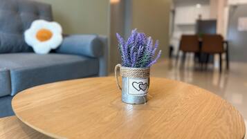 Una sala de estar con una mesa redonda de madera, un sofá gris y una planta decorativa en una maceta con forma de corazón.