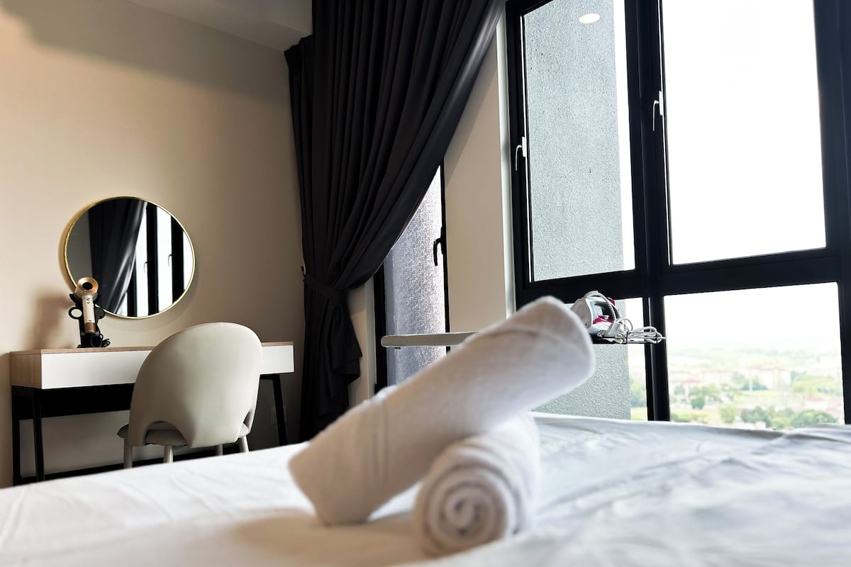 Quarto de hotel com cama, escrivaninha, cadeira, espelho e janela com vista.