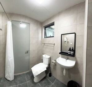 A modern bathroom with a glass shower enclosure, a toilet, a sink, and a mirror with a mounted shelf above it. - Tulip Residences by Manhattan Group (Shah Alam)