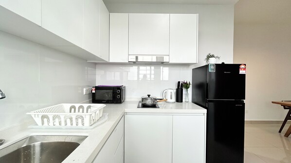 A compact kitchen with white cabinets, a black refrigerator, a microwave, and a sink. - Tulip Residences by Manhattan Group (Shah Alam)