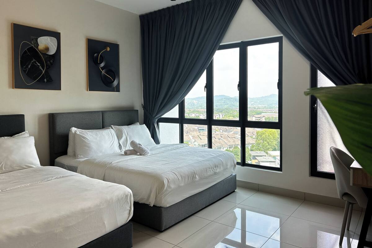 Quarto de hotel com duas camas, ventoinha no teto, janelas amplas com cortinas e obras de arte nas paredes.