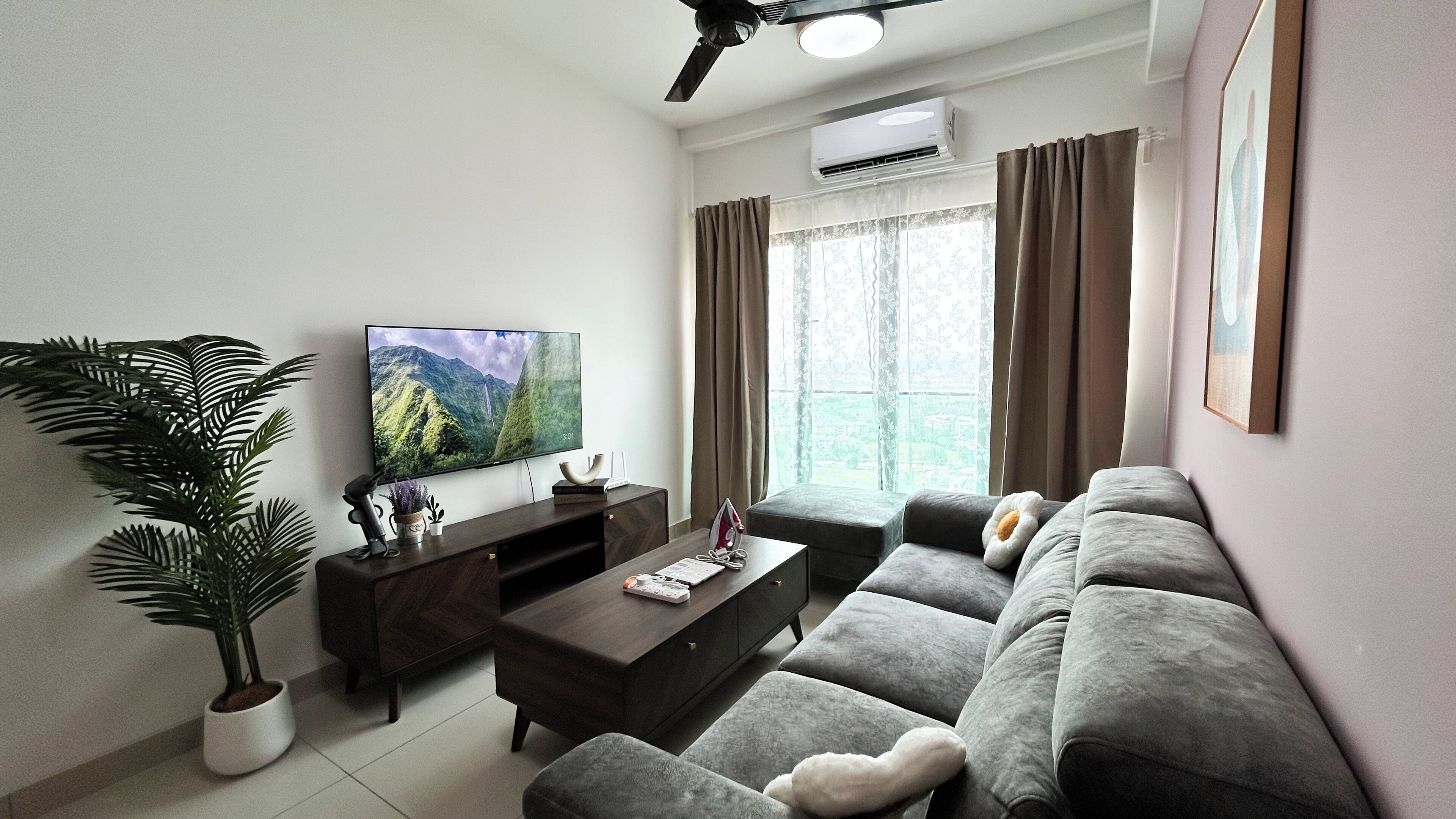 A modern living room with a flat-screen TV, a sofa, a coffee table, and a potted plant.