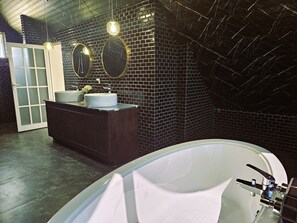 A modern bathroom with a black tiled wall, a white bathtub, and a dark wooden vanity with two round mirrors.