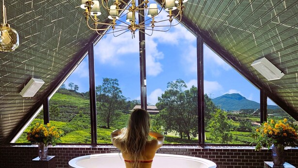 A room with a large bathtub, a chandelier, and a view of a green landscape through large windows. - Private Villa by the Tea Estate (Nuwara Eliya)