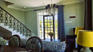 A dining area with a chandelier, patterned upholstery, and a staircase with decorative railings. - Private Villa by the Tea Estate (Nuwara Eliya)