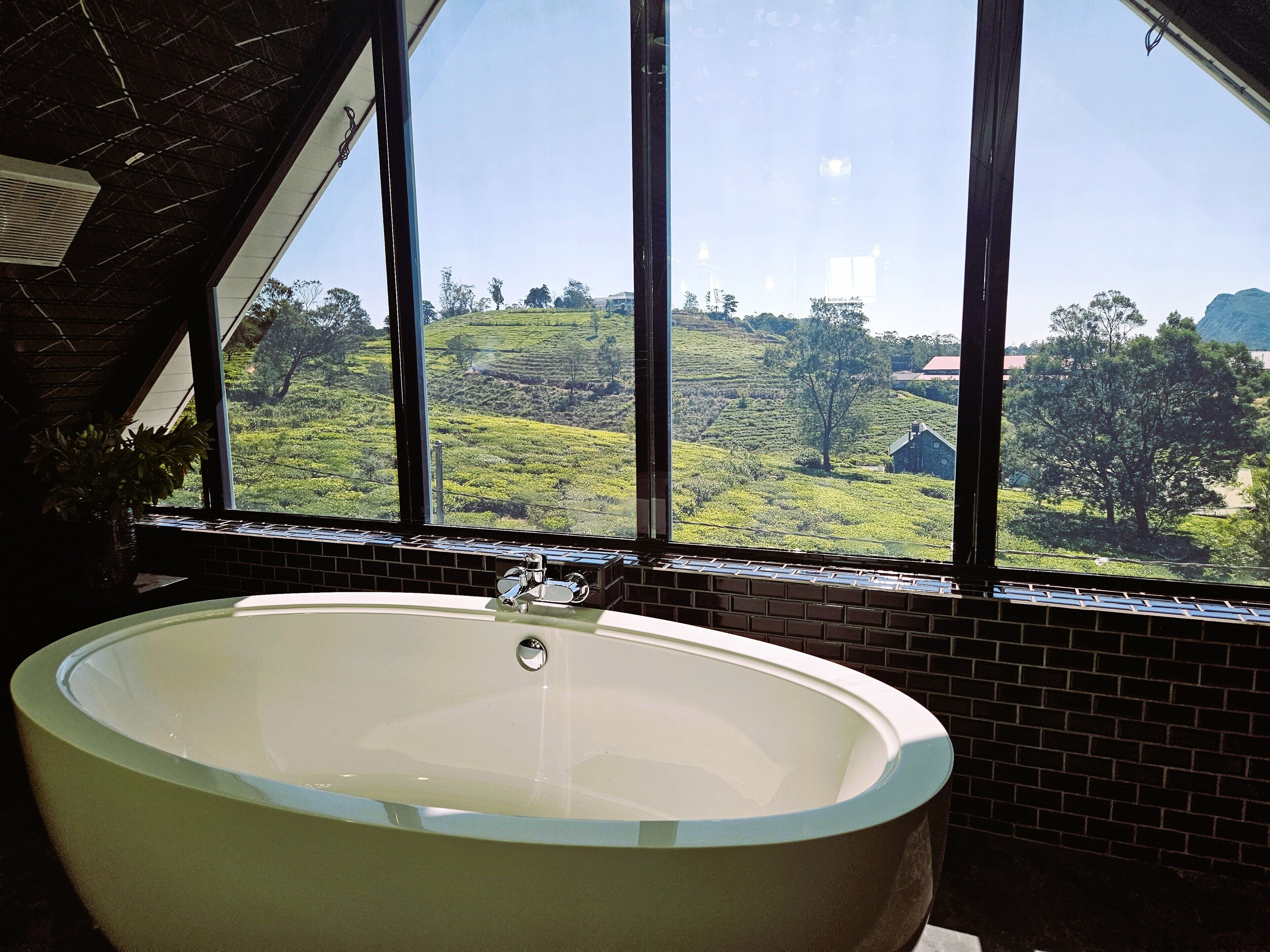 A large bathtub in a room with a view of a green landscape through large windows.