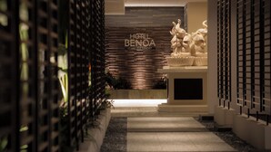 A modern hotel entrance with a stone facade, a reception desk, and a decorative sculpture. - Hotel Benoa Resort (Kobe)