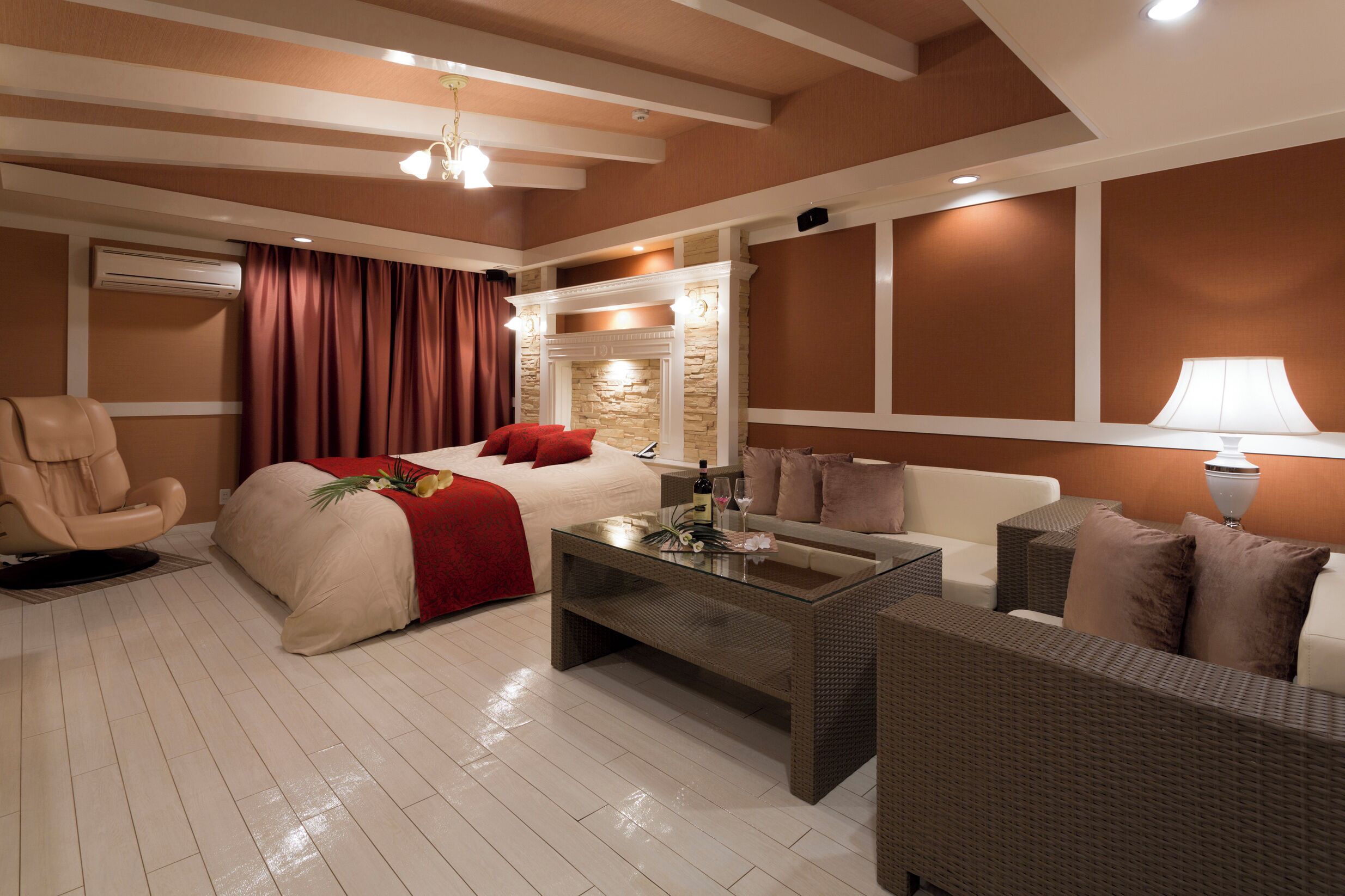 A modern hotel room with a bed, a sofa, a glass coffee table, and a fireplace.
