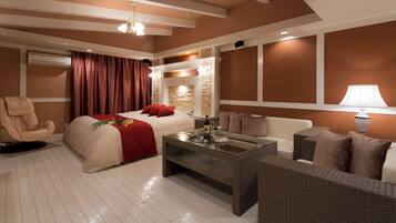 A modern hotel room with a bed, a sofa, a glass coffee table, and a fireplace.