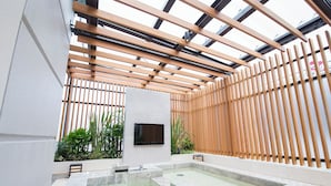 A spa area with a wooden slatted ceiling, a flat-screen TV, and a rectangular hot tub. - Hotel Benoa Resort (Kobe)