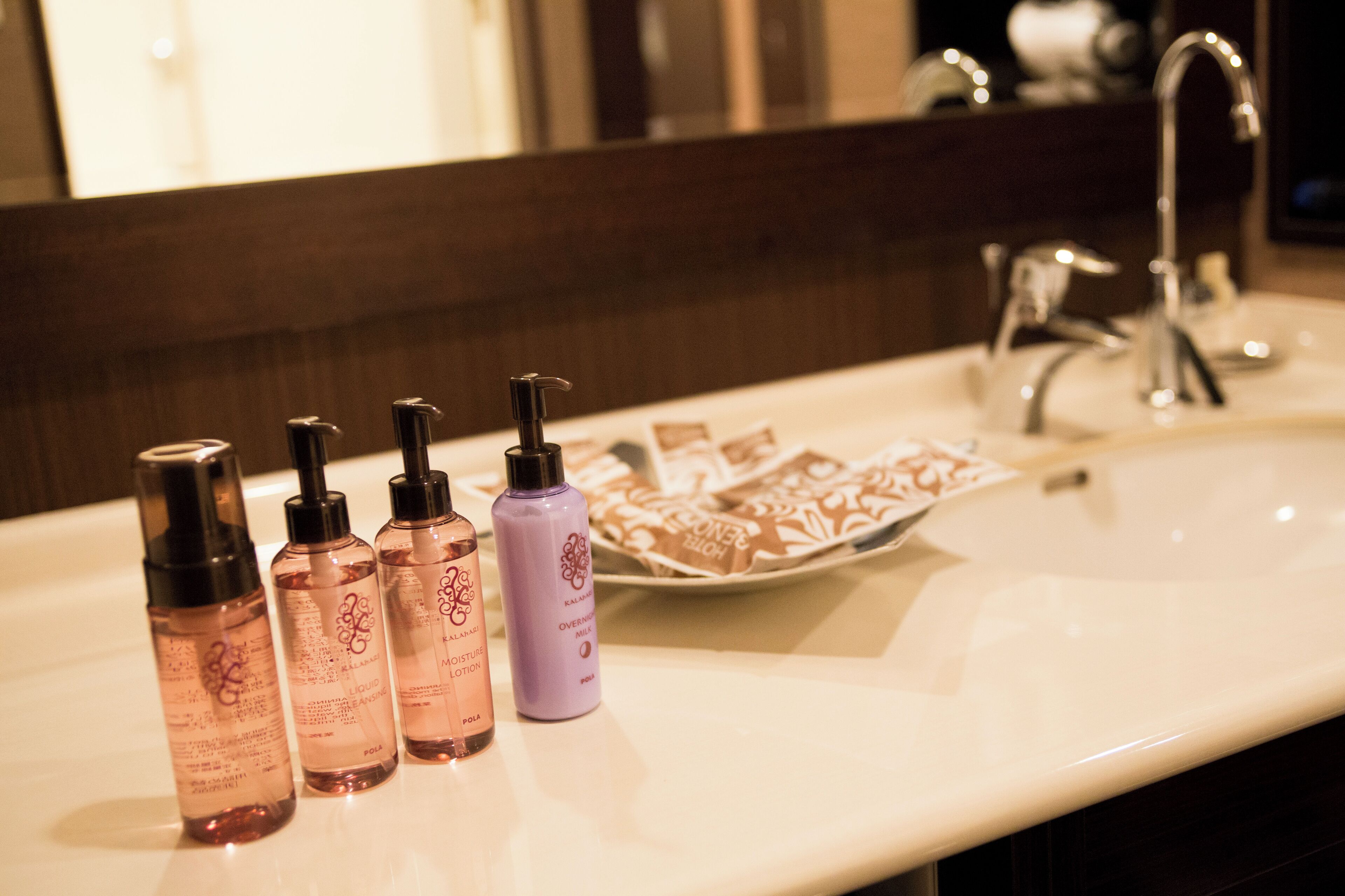 A bathroom with a white sink, a mirror, and four bottles of lotion.