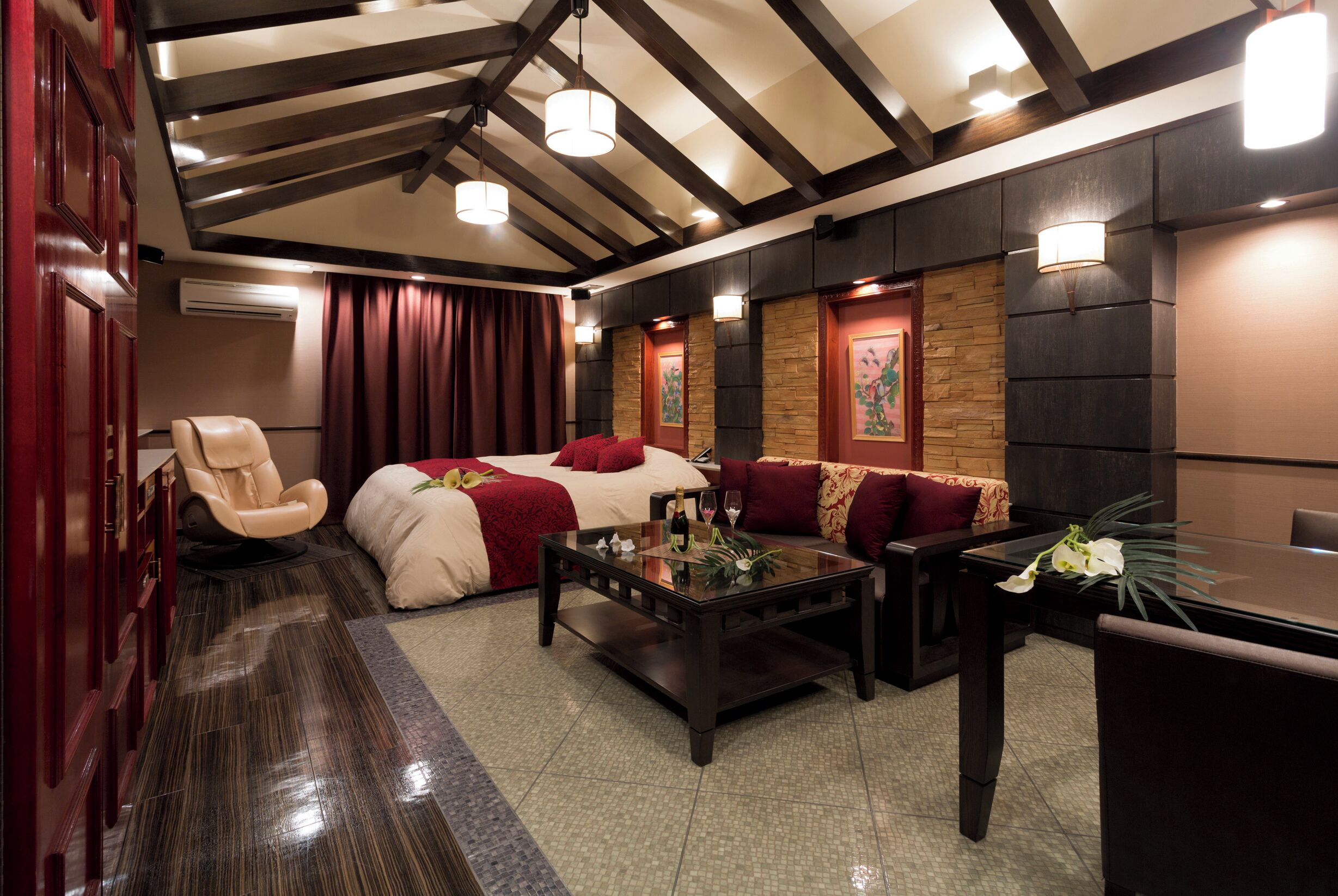 A hotel room with a bed, a massage chair, a coffee table, and a seating area with a table and chairs.
