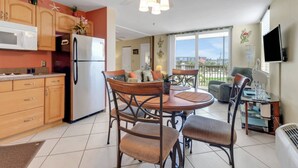 A compact kitchen with a refrigerator, microwave, and wooden cabinets. There is a dining area with a table and chairs, and a balcony with a view of the city. - GULF VIEW | 3RD FLOOR STUDIO | KING BED + QUEEN SLEEPER | FREE WIFI | STEPS TO BONITA BEACH (Bonita Springs)