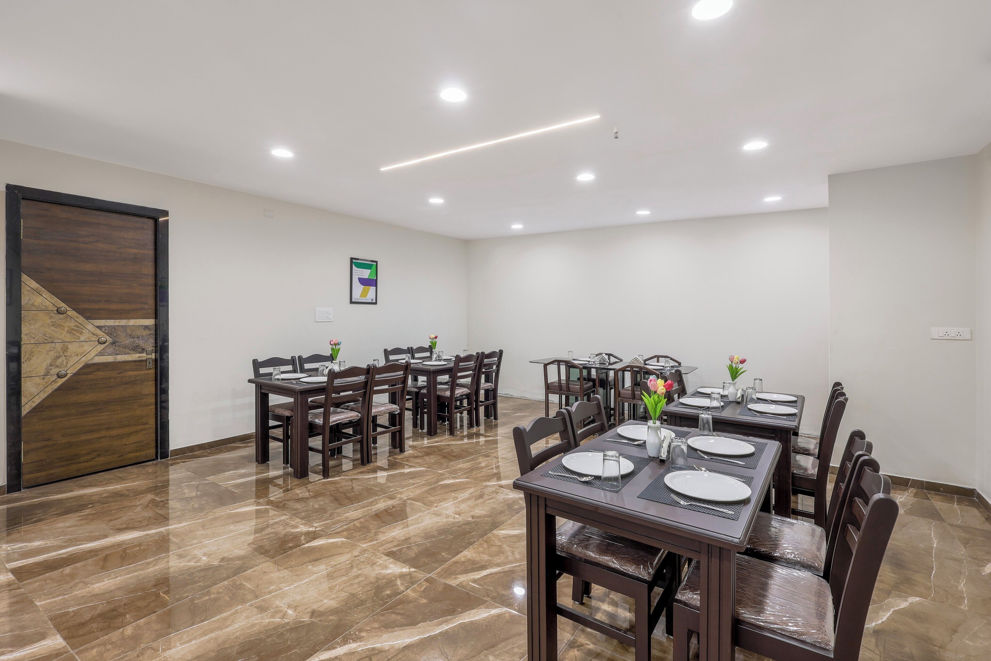 A dining area with multiple tables and chairs, a wooden door, and recessed ceiling lights.