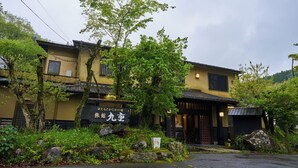 Een traditioneel Japans gebouw met een bordje, omgeven door weelderige begroeiing en rotsen.