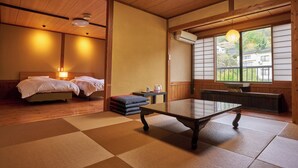 Een traditionele Japanse kamer met tatami vloerbedekking, een lage tafel, twee bedden en uitzicht op een woonwijk door een groot raam.