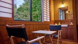 Een houten cabinemeubilair met een eettafel en stoelen, een raam met uitzicht op bomen, en een badkamer met spiegel en wastafel.