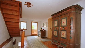 Ein Zimmer mit einer Holztreppe, einem großen Holzschrank mit floralen Verzierungen und Blick nach draußen durch eine Tür.