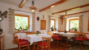 Ein Essbereich mit Holztischen und -stühlen, weißen Tischdecken und roten Kissen.