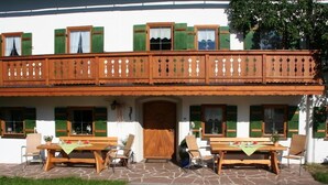 Ein traditionelles Chalet mit Holzbalkon, Steinböden und Sitzgelegenheiten im Freien.