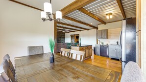 Een ruime eetruimte met een houten tafel en stoelen, een kroonluchter en uitzicht op een keuken met moderne apparatuur.