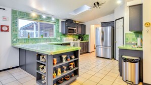 Une cuisine moderne avec un mur recouvert de carreaux verts, des appareils électroménagers en acier inoxydable et une étagère intégrée où sont exposés des objets décoratifs.