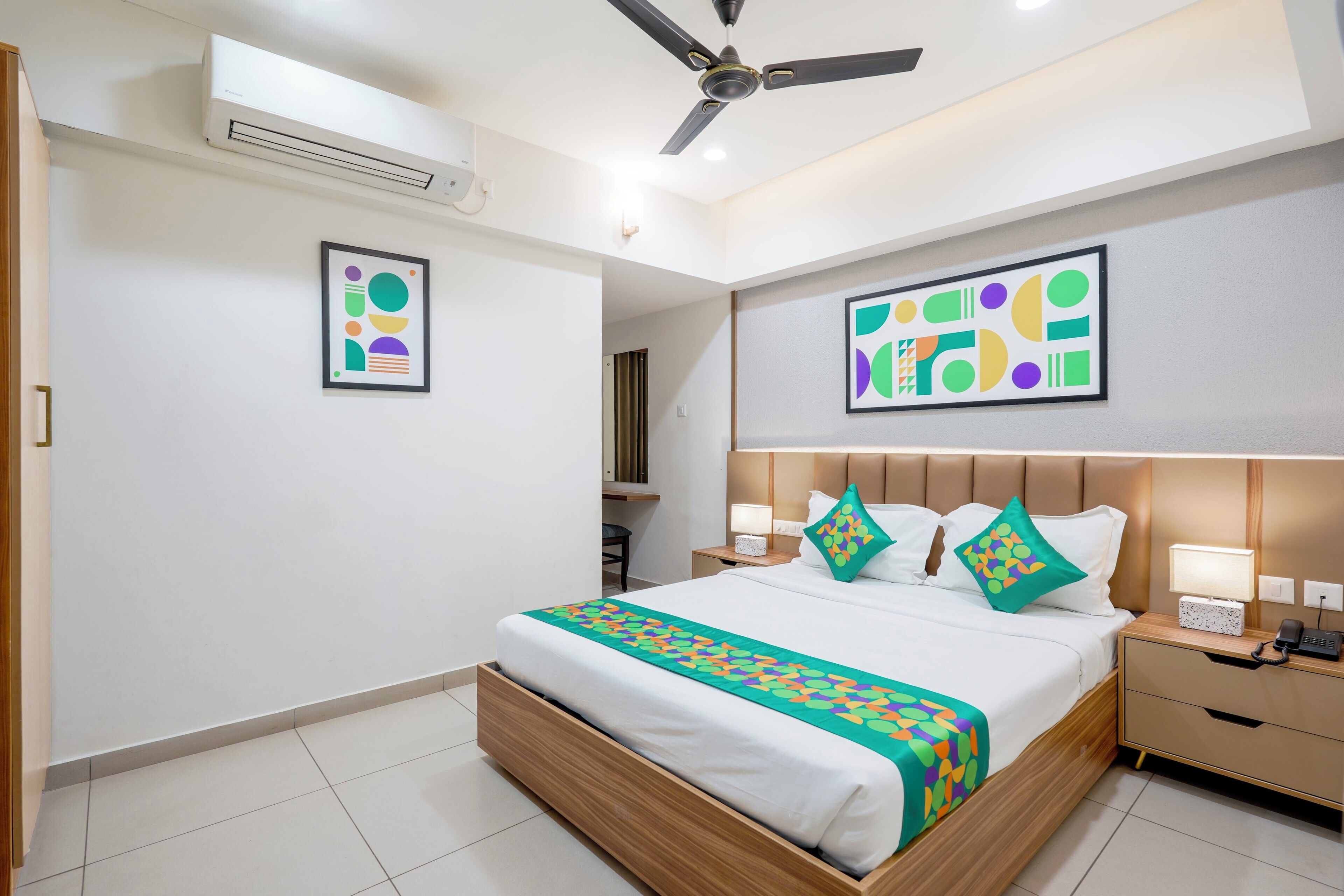 A modern hotel room with a large bed, bedside tables, a ceiling fan, and artwork on the walls.
