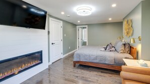 A bedroom with a fireplace, a bed, a TV mounted on the wall, and a ceiling light. - Family Friendly: Modern Apt in Fort Washington (Fort Washington)