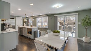 A modern kitchen with a central island, white cabinetry, and a dining area with a large table and chairs. - Family Friendly: Modern Apt in Fort Washington (Fort Washington)