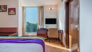Ein Hotelzimmer mit Bett, Schreibtisch, Stuhl, Fernseher und einem Fenster mit Vorhängen.