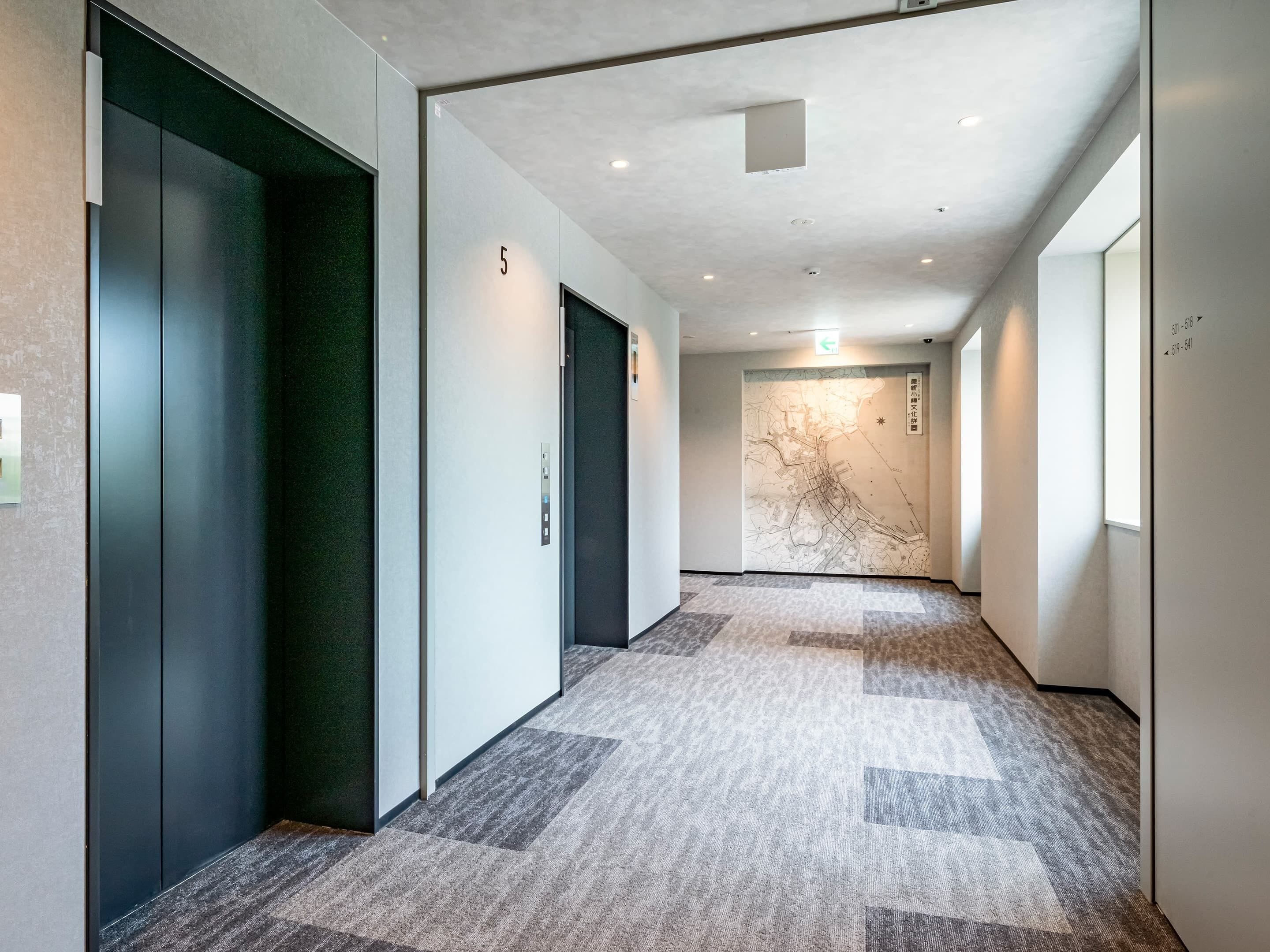 A hallway with carpeted flooring, a map on the wall, and doors marked with numbers.