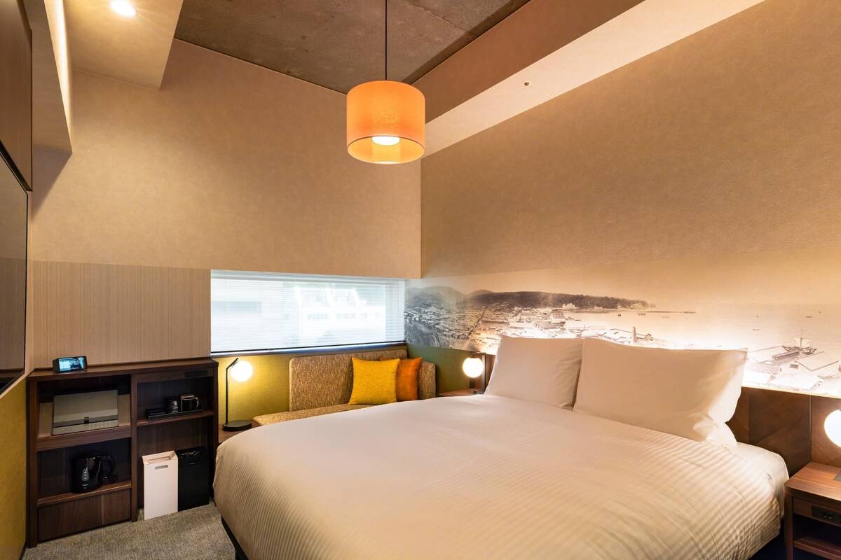 A modern hotel room with a large bed, a desk with a computer, a small seating area, and a view of the sea.
